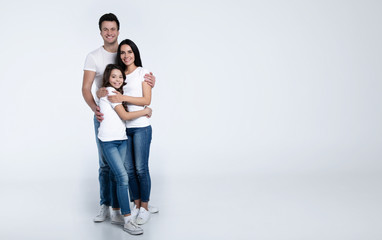 Beautiful excited and the funny family team is posing and pointing in a white t-shirt while they isolated on white background in studio.