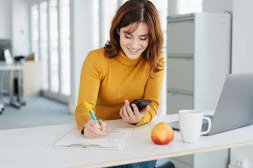 Smiling young businesswoman sitting writing notes