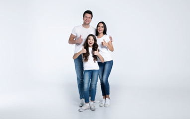 Beautiful excited and the funny family team is posing and pointing in a white t-shirt while they isolated on white background in studio.