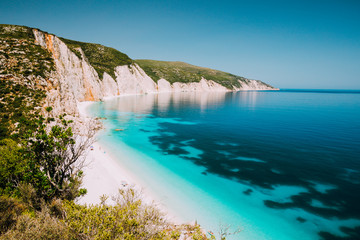 Fototapeta premium Holiday vacation. Fteri beach, Kefalonia, Greece. Calm clear blue emerald green turquoise sea with dark deep pattern and rocky coastline in background