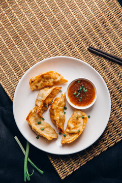 Asian dumplings Gyozas potstickers fried on cast-iron pan, served with chopsticks and bowl of soy sesame sauce over black texture background. Top view, space...N.