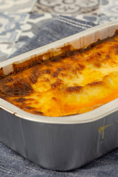 Beef lasagne or lasagna ready bfrozen meal cooked in a metal baking tray on a blue tea towel.  Fast food concept