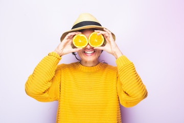 Young funny Caucasian woman, with yellow sweater and  with two orange slices in his eyes posing funny at the photo studio.