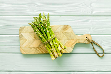Cooking asparagus. Bunch steams on cutting board on green wooden background top-down