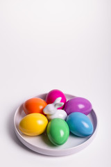 Six Easter eggs in yellow, orange, pink, violet, green, blue colors in the white porcelain plate with white Easter bunny on white background. Selective focus. Easter card. Happy Easter!