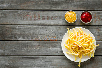 Potato chips on plate near sauces on dark wooden table top-down copy space