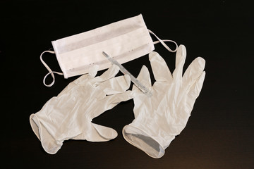 Two latex gloves, thermometer and mask close-up on black background