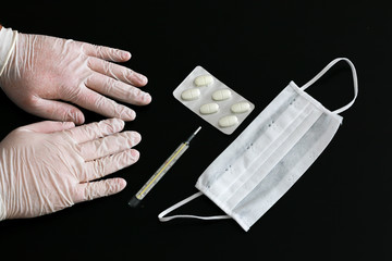 Two hands in latex gloves, thermometer, pills and medical mask