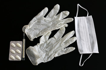 Latex gloves, thermometer, pills and medical mask on black background