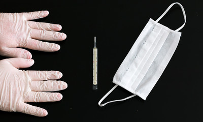 Two hands in latex gloves, thermometer and medical mask