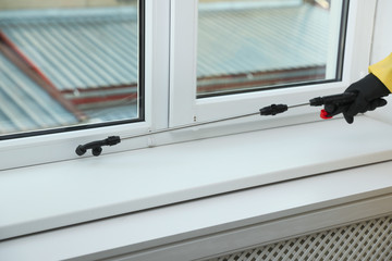Pest control worker in protective suit spraying insecticide on window sill indoors, closeup