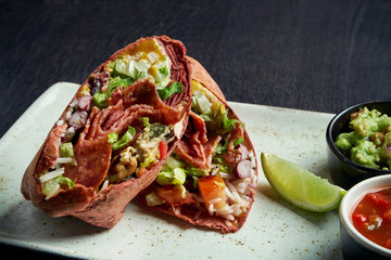 Close up view on burrito with salami chorizo, rice, tomatoes, corn and bell pepper in brown pita on a brown plate with tomato salsa and guacamole. Vegetarian Shawarma Roll