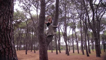 The Barefooted Woman Posing In Grande Battement With Hands In Fifth Position On Top Of The Tree. -wide shot