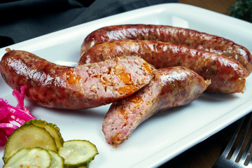 Appetizing juicy pork minced sausage baked in a smoker with cheddar in a white plate with canned vegetables. German beer snack
