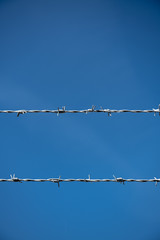 Two rows of Barbed Wire in front of blue sky.