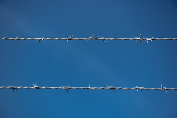 Two rows of Barbed Wire in front of blue sky.