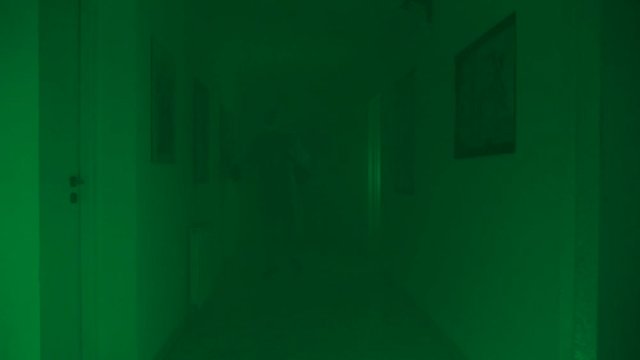 Man in protective suit in long hazy corridor sprays disinfectant liquid on walls; flashing green light