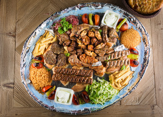 Full view of Persian Mix Kebab of minced meat and chicken With Rice and french fries and vegetables in a large traditional tray on wooden table