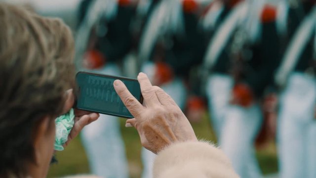 Taking a picture with the smartphone of marching soldiers in beautiful uniform in slow motion.