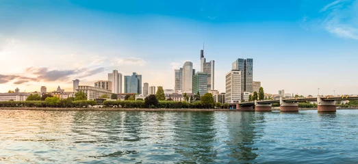 Panoramablick auf die Skyline von Frankfurt am Main mit Touristenboot, Promenade und Wolkenkratzern über dem Main bei Sonnenuntergang © Julia Lavrinenko