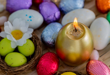 Obraz na płótnie Canvas Festive easter concept of candle and colorful eggs on a wooden table. Daisy flower, green eggs in the nest. Greeting card Easter.