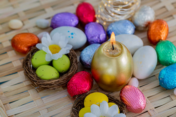 Festive easter concept of candle and colorful eggs on a wooden table. Daisy  flower, green eggs in the nest. Greeting card Easter.