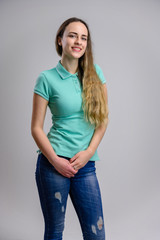 Vertical photo of a pretty girl with long beautiful hair with a smile in a turquoise blouse and blue jeans on a white background.