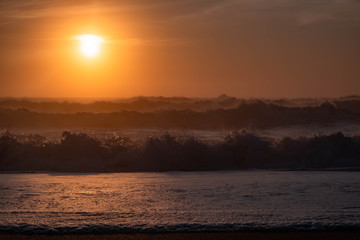 Landscape of Beautiful Orange Sunset Over Flowing and Crashing Ocean Waves at the Beach in Nazare, Portugal