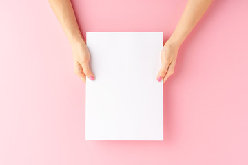Woman’s hands holding empty white paper sheet on pink background. Close up