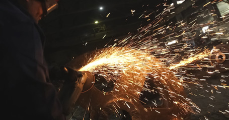 Working in a mask and headphones cleans joints angle grinder on metal parts blanks