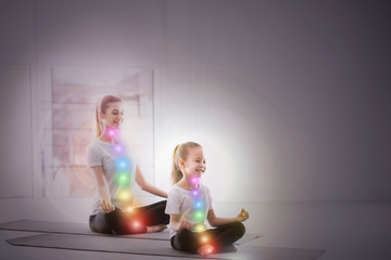 Mother and daughter with chakra points practicing yoga in studio. Healing energy