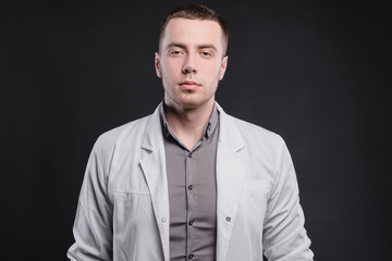 Young, pretty man in a medical coat on a gray background. The concept of medical education and medical activity
