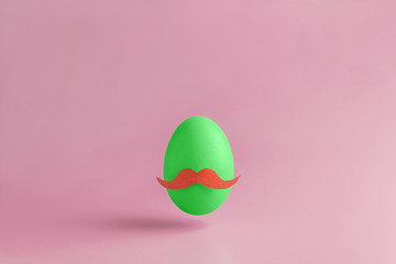 One green egg with mustache on a pink background. Minimal Happy Easter concept decoration. Copy space for text mockup.
