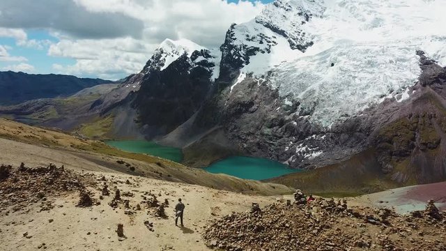 Aerial, pull back, drone shot of Ausangate mountain and the double lakes, revealing a man on top of a hill, in Cusco region, Peru, South America
