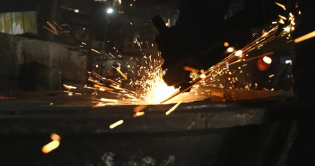 Working in a mask and headphones cleans joints angle grinder on metal parts blanks