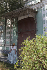 Look of russian girl in beautiful retro dress, vintage hat and porch door of old house in Astrakhan...