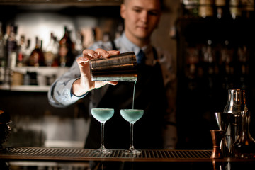 Close-up bartender pours cocktail from shaker into glass.