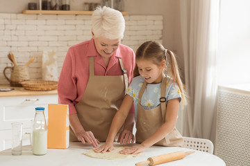 Mature woman and her grandchild making dough for baking indoors