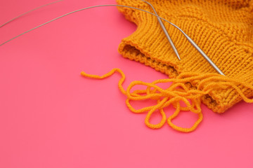 Knitting wool sweater and knitting needles on pink background, copy space