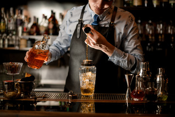 Professional barman using beaker pours drink into glass shaker