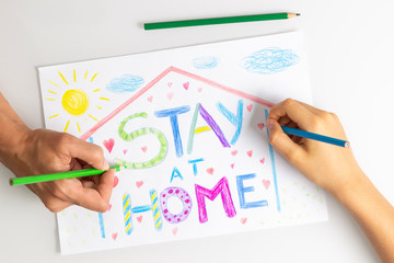 Quarantine at home during coronavirus pandemic. Kid and mother hands drawing with coloring pencils picture with words Stay at home. Social media campaign for coronavirus prevention