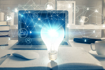 Computer on desktop in office with bulb icon hologram. Multi exposure. Concept of idea.