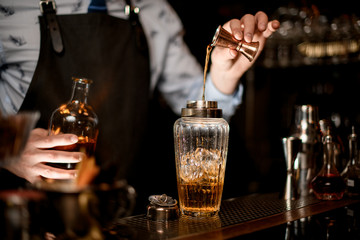 Close-up bartender using beaker pours drink into glass shaker
