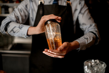 bartender hold by two hands glass shaker with cocktail.