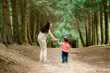 Fototapeta premium Backview of Mother walking with cute son in summer park. Happy woman with cheerful little boy outdoors