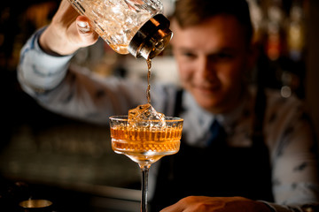 close-up of glass in which bartender pours finished cocktail.