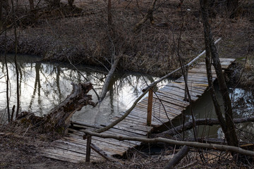 Fototapeta na wymiar Old rustic wooden bridge over a small river - very dark atmosphere