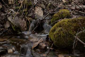 A beautiful small waterfall in a thicket of forest on high hills among huge boulders covered with moss