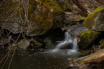 A beautiful small waterfall in a thicket of forest on high hills among huge boulders covered with moss