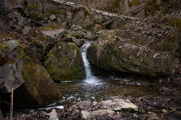A beautiful small waterfall in a thicket of forest on high hills among huge boulders covered with moss